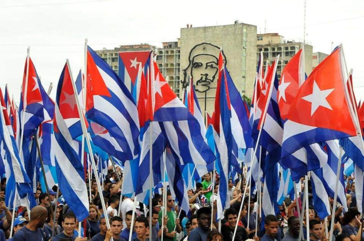 Multitud ondeando banderas de Cuba en la Plaza de la Revolución con la imagen del Che Guevara de fondo.