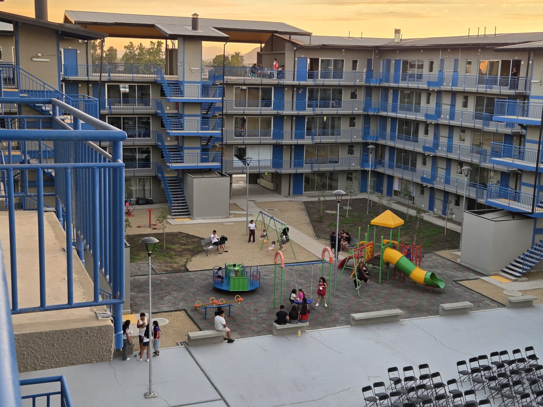 Patio interior del Barrio Maestranza Ukamau 2 al atardecer, con juegos infantiles y vecinos